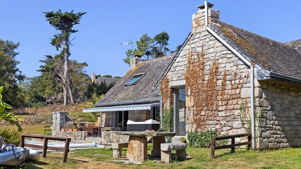 A stone building with a sloped roof, a wooden bench, and a boat in the foreground. - Holiday Home 'Maison Bringwiller Plage 200m' with Private Pool and Terrace (Trégastel)