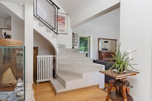 A spacious living area with a staircase leading to an upper level, a large window, and a view of greenery outside.