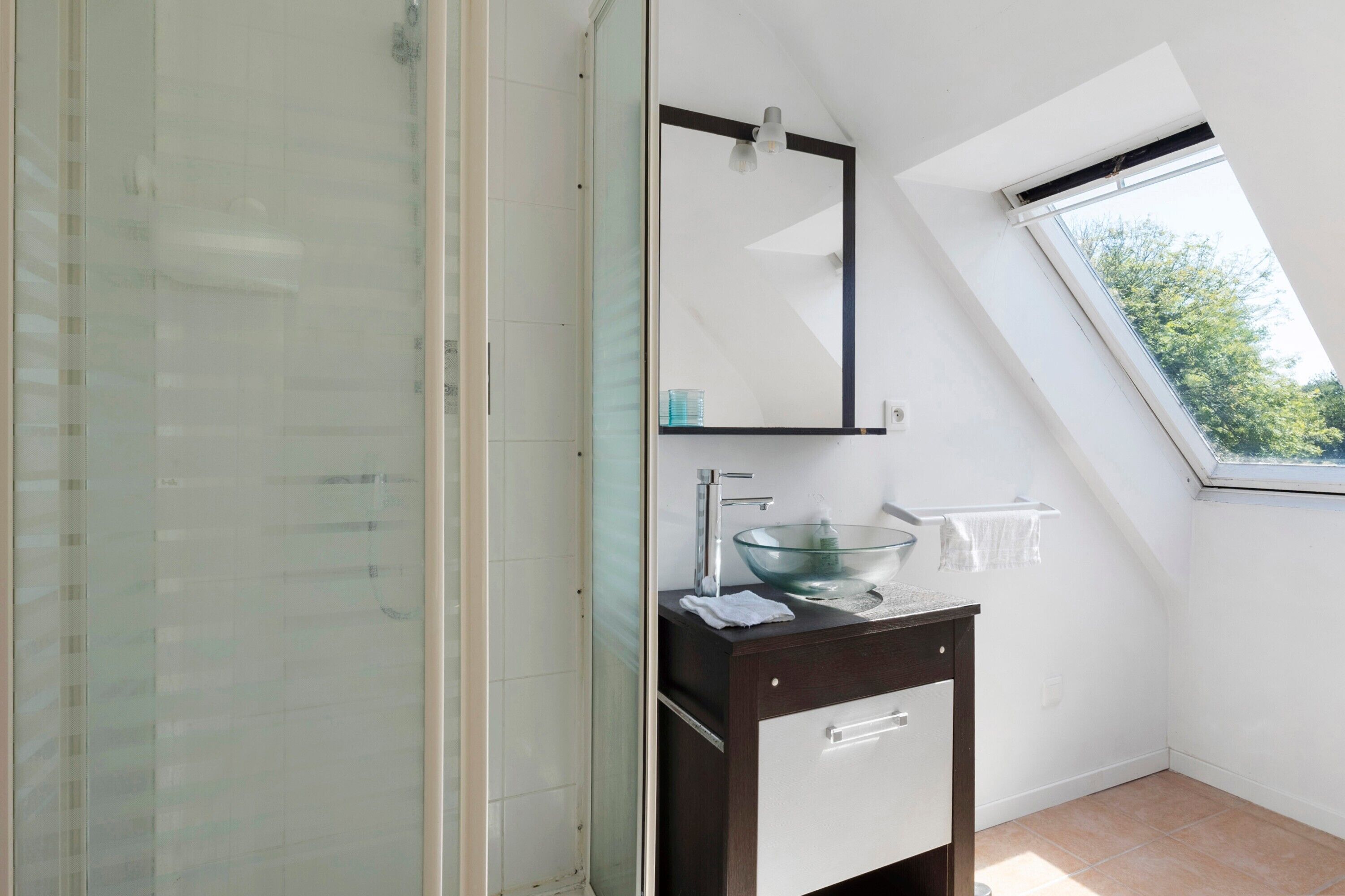 A modern bathroom with a glass-enclosed shower, a glass bowl sink, and a skylight.