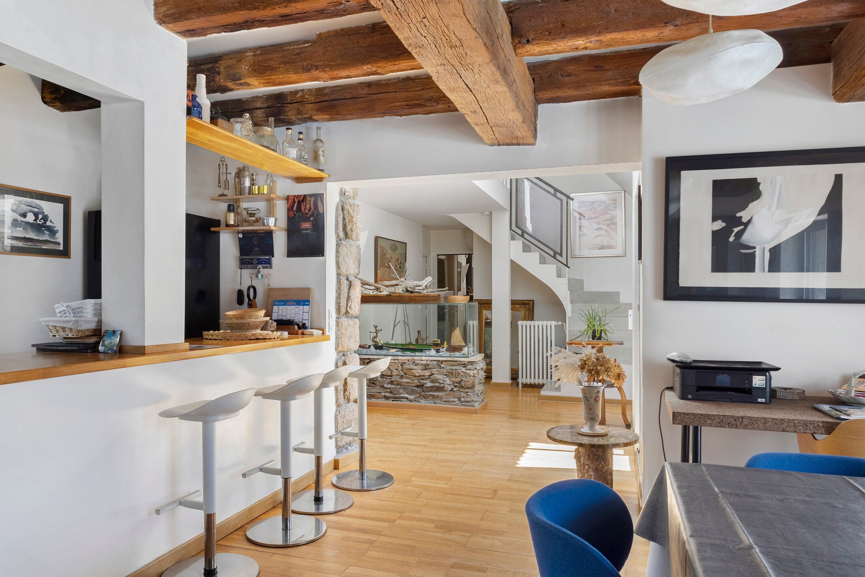 A modern interior with a kitchen area, bar stools, a dining table, and a staircase leading to an upper level.