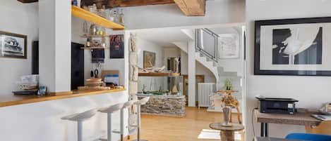 A modern interior with a kitchen area, bar stools, a dining table, and a staircase leading to an upper level.