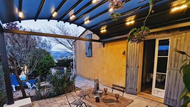 An outdoor patio with a table and chairs, a pergola with lights, a door, and a view of the landscape. - 'Bel Air en Luberon' Cottage with Shared Pool and Panoramic Luberon Views (Gargas)