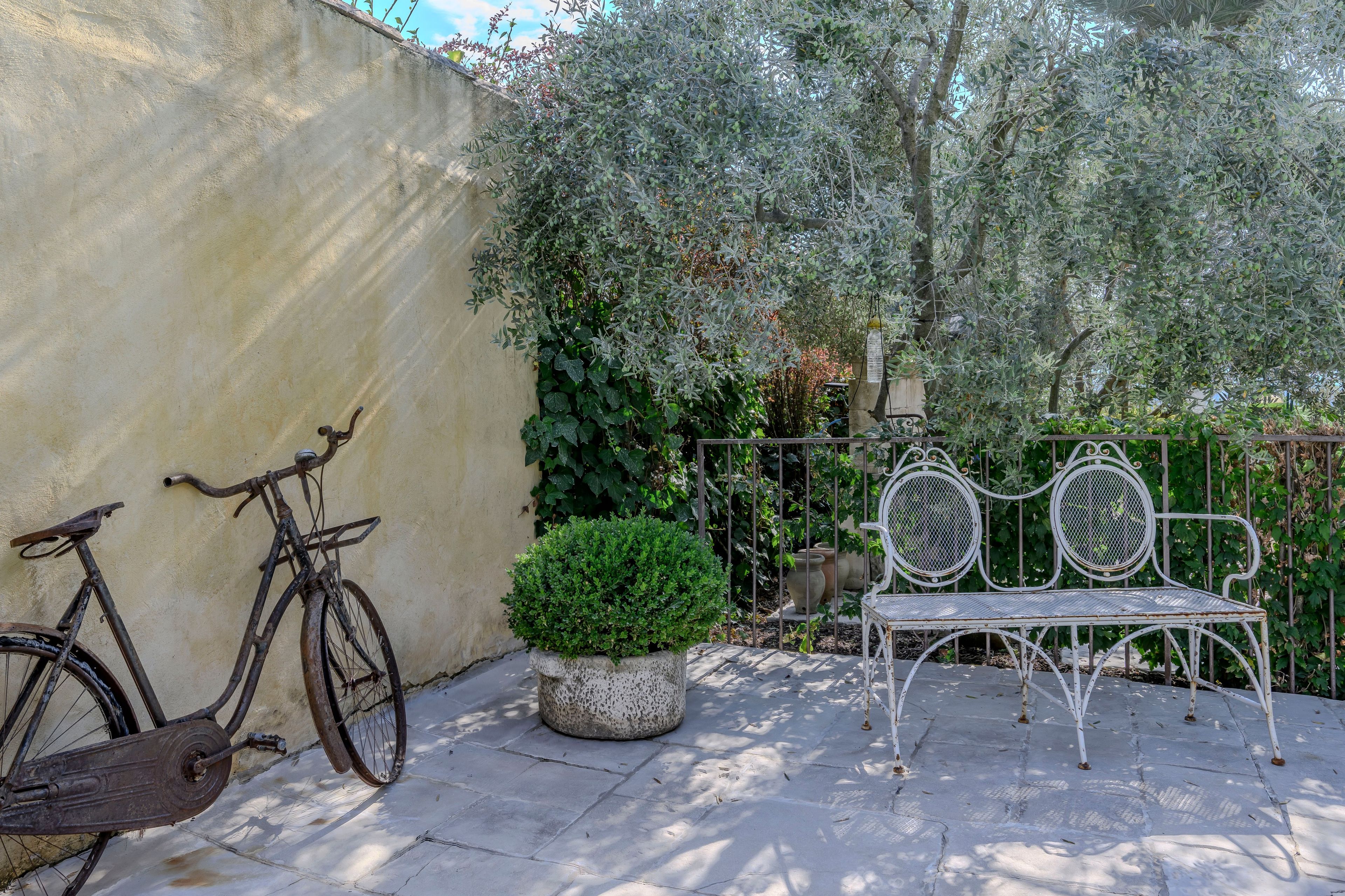 A patio with a metal bench and a bicycle leaning against a wall.