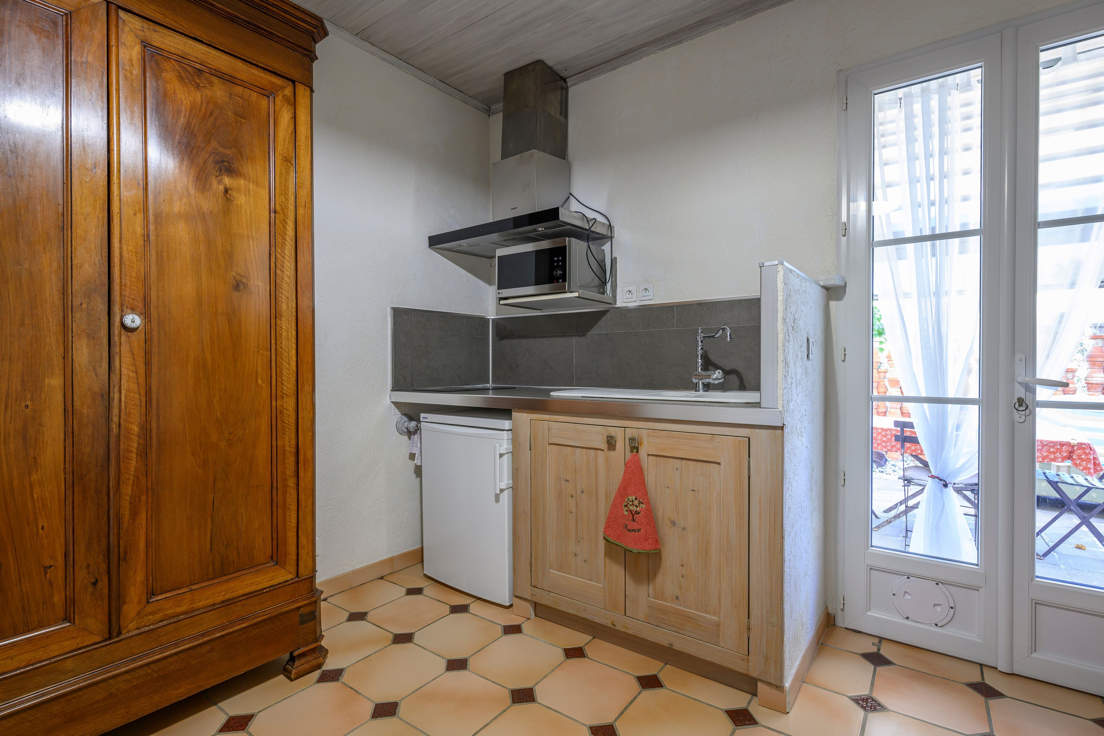 Une cuisine compacte avec un meuble en bois, un four à micro-ondes, un petit réfrigérateur et un sol carrelé.
