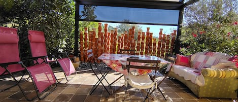 Un patio exterior con mesa y sillas, un área de estar cubierta y una pared decorativa de macetas de terracota.