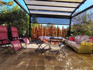 Un patio exterior con mesa y sillas, un área de estar cubierta y una pared decorativa de macetas de terracota.