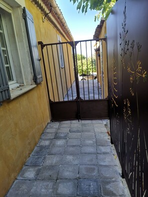 Una entrada cerrada con un camino de piedra que lleva a un edificio de pared amarilla y una ventana con persianas.