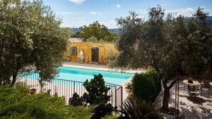 A pool area with a statue, a yellow building, and surrounding greenery. - 'Bel Air en Luberon' Cottage with Shared Pool and Panoramic Luberon Views (Gargas)