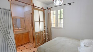 A bedroom with a bed, a window, a door, and a bathroom with a mirror and sink. - 'Bel Air en Luberon' Cottage with Shared Pool and Panoramic Luberon Views (Gargas)