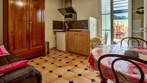 A compact kitchen with a microwave, stove, and sink, a wooden cabinet, and a dining area with a table and chairs. - 'Bel Air en Luberon' Cottage with Shared Pool and Panoramic Luberon Views (Gargas)