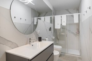 A modern bathroom with a marble sink, a large mirror, a glass shower enclosure, and a toilet.