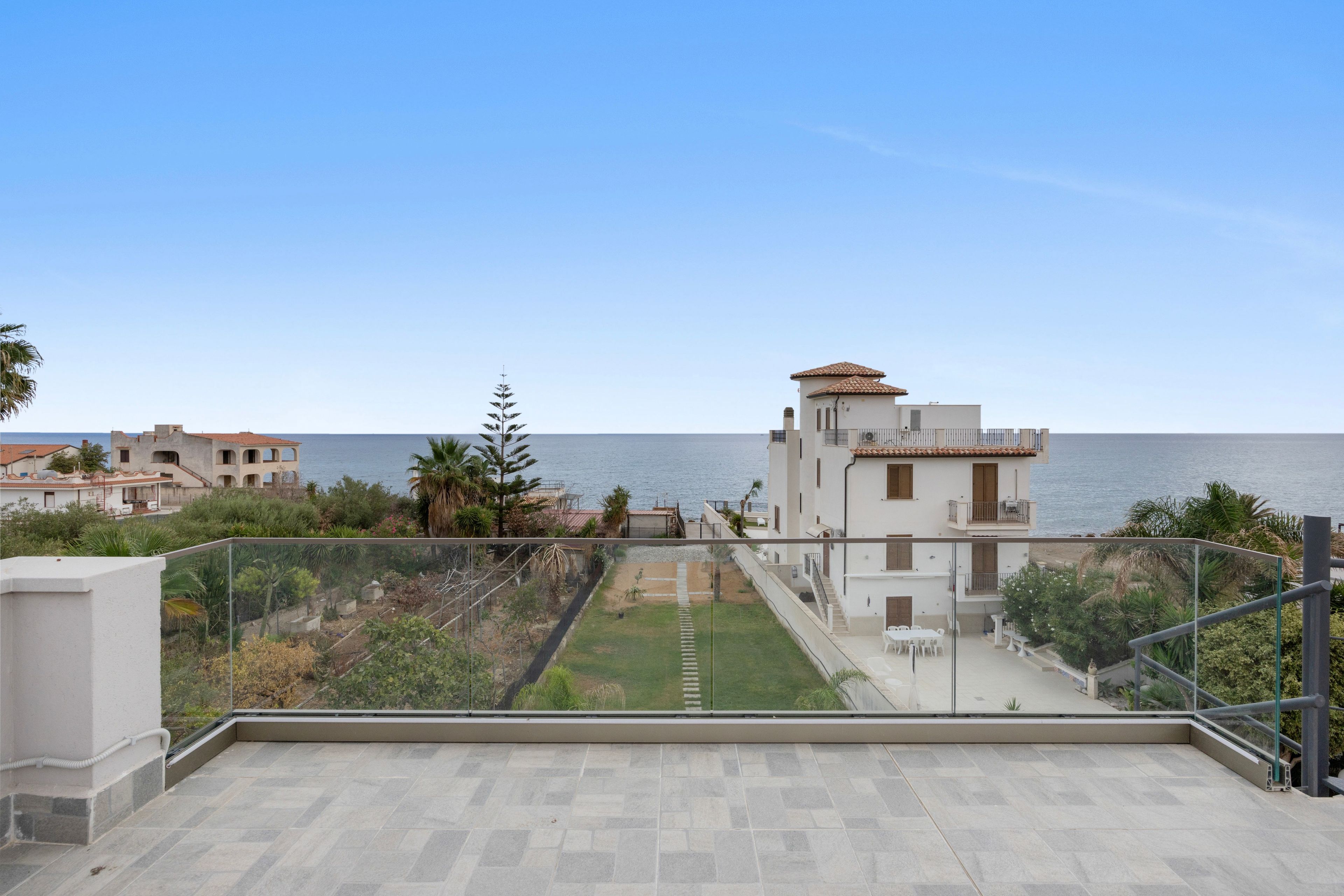 A residential building with a view of the sea, a garden area, and a balcony with a glass railing.