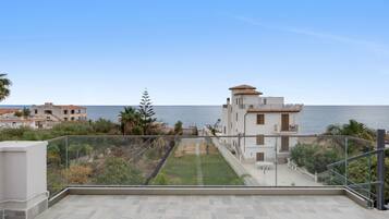 A residential building with a view of the sea, a garden area, and a balcony with a glass railing.