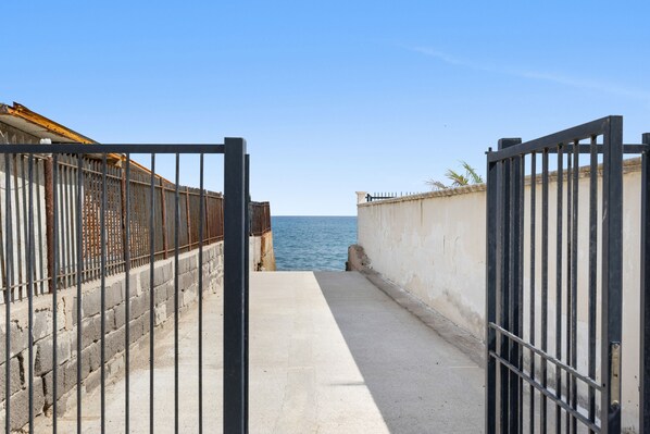 A pathway leading to a body of water, flanked by metal gates and a concrete wall.