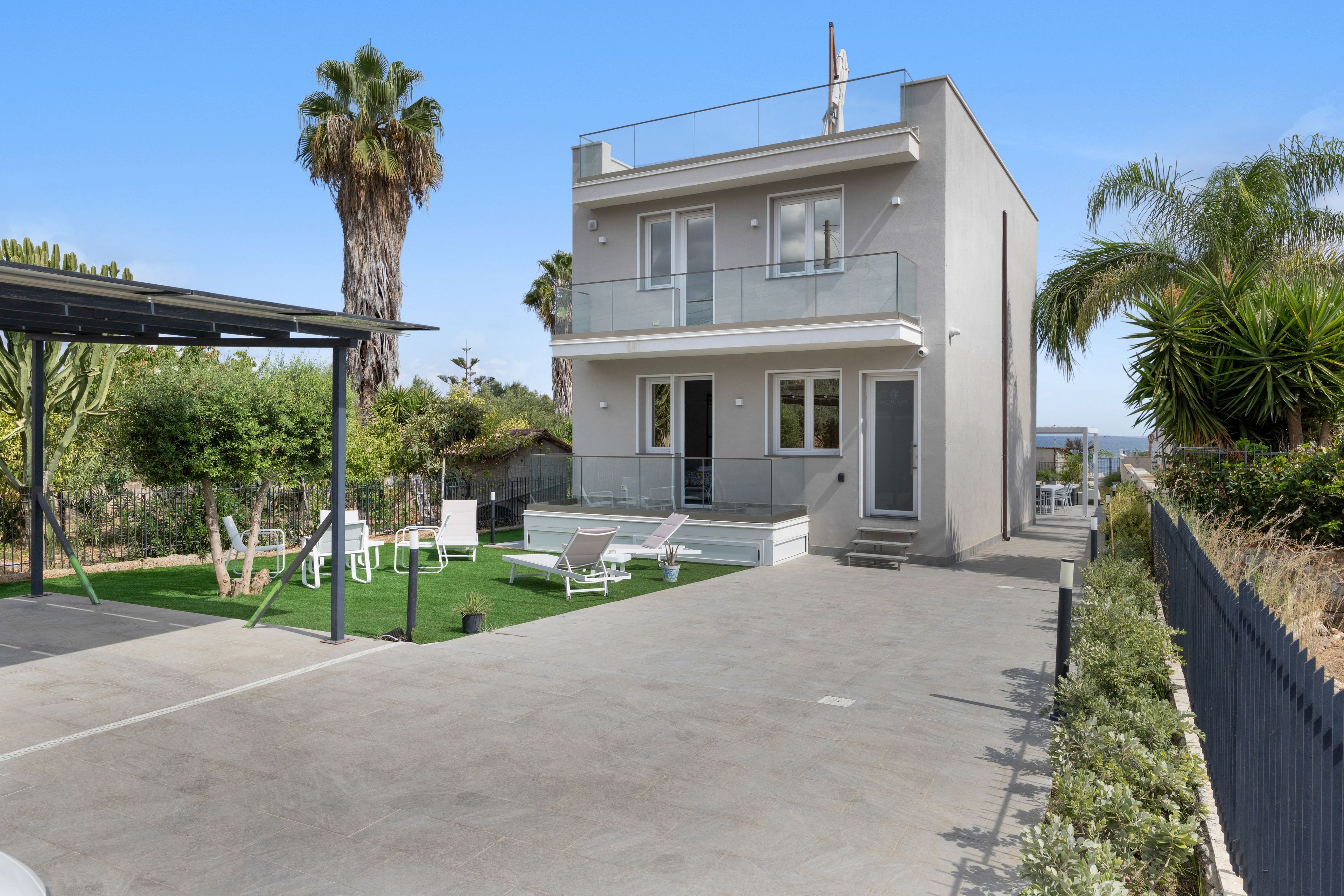 Ein modernes, zweistöckiges Haus mit überdachter Terrasse, Sitzgelegenheiten im Freien und Blick auf den Ozean.