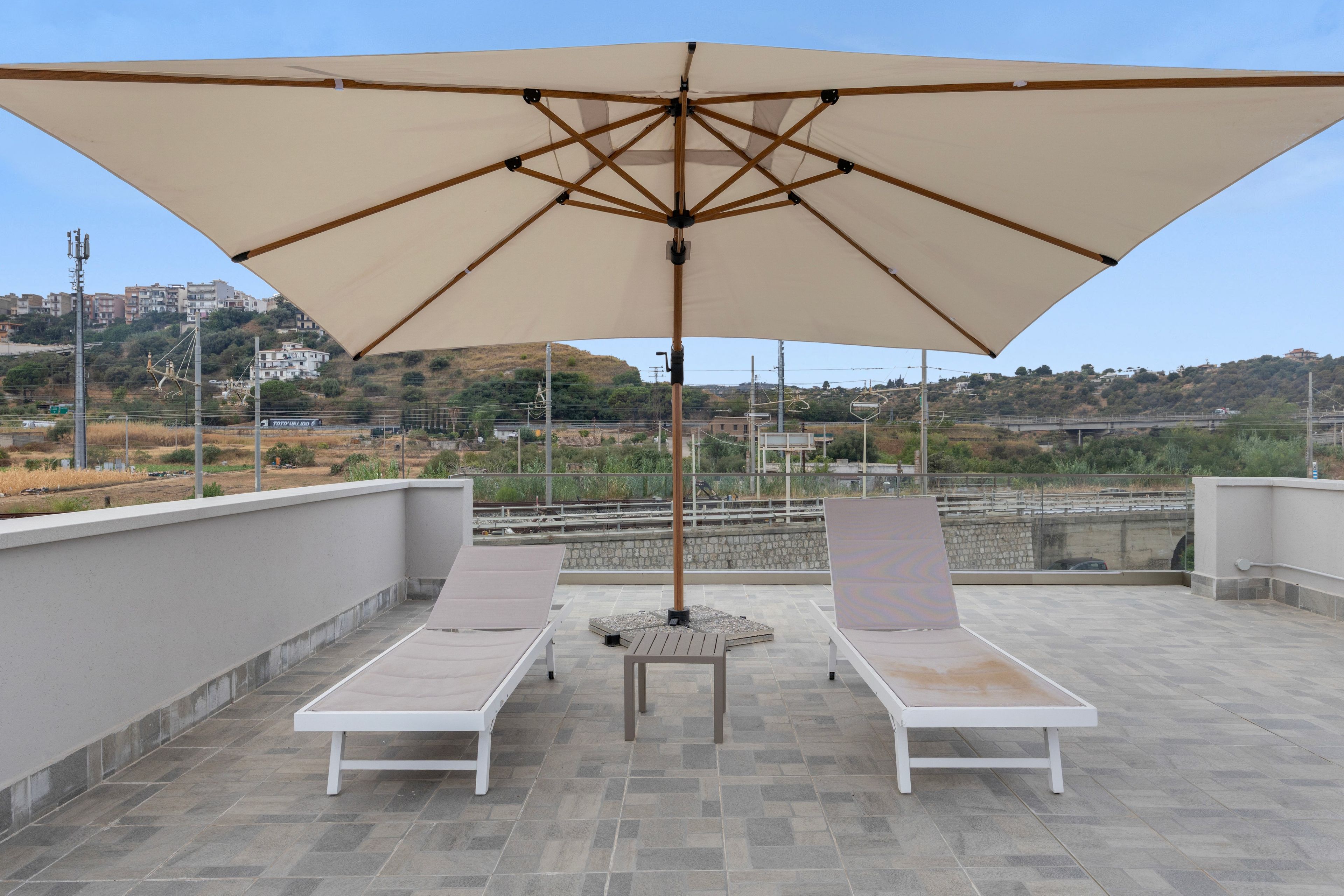 A rooftop terrace with two lounge chairs, a table, and a large umbrella.