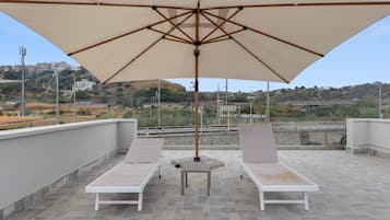 A rooftop terrace with two lounge chairs, a table, and a large umbrella.
