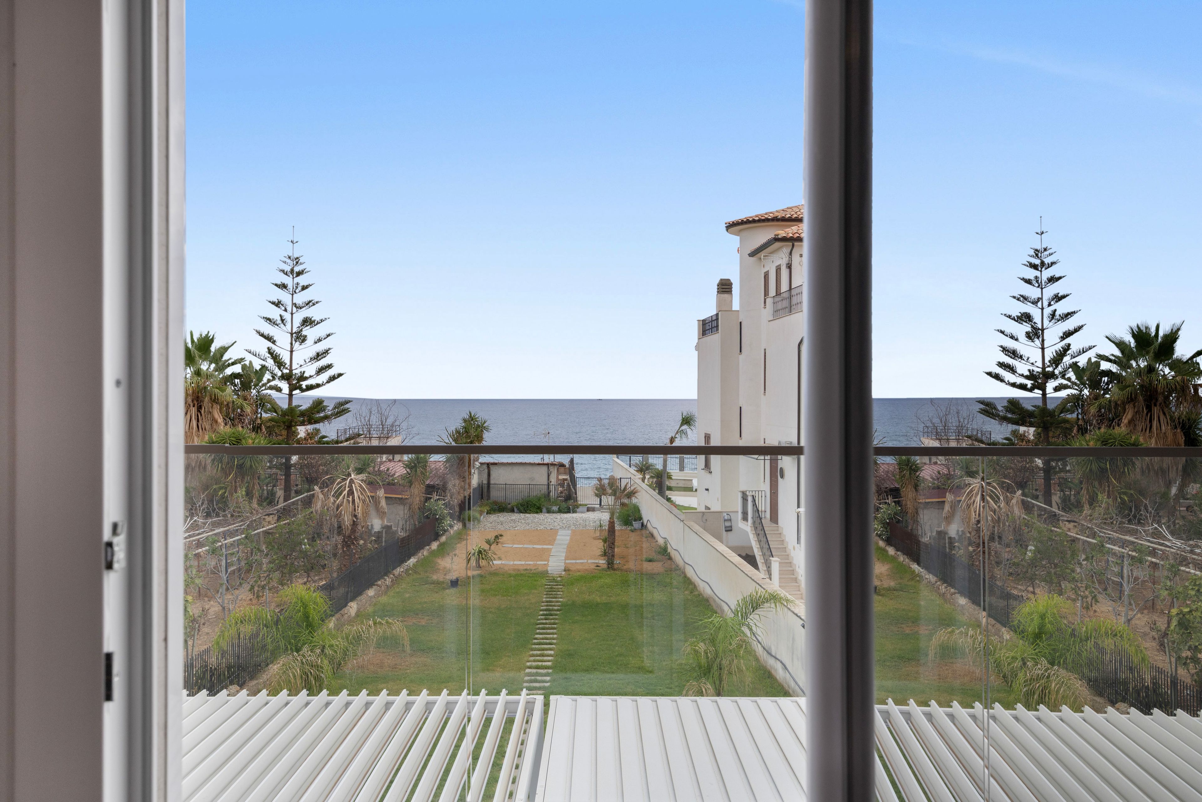 Ein Balkon mit Blick auf eine Küstenlandschaft, inklusive eines Gebäudes mit einem Turm und einem klaren Himmel.