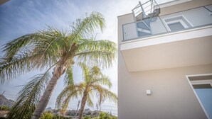 Un bâtiment moderne doté d’un balcon, de palmiers et surplombant un ciel dégagé.