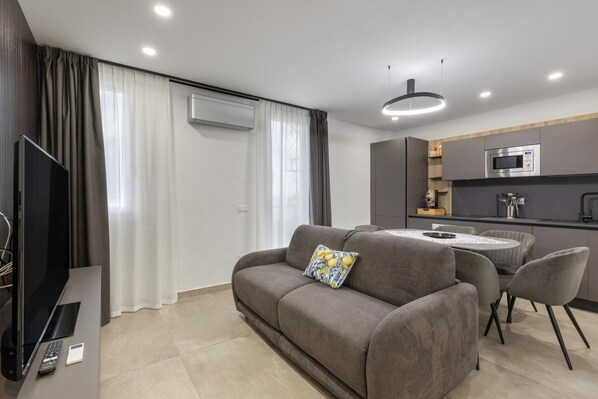 A modern living room with a sofa, a TV, and a dining area with chairs.