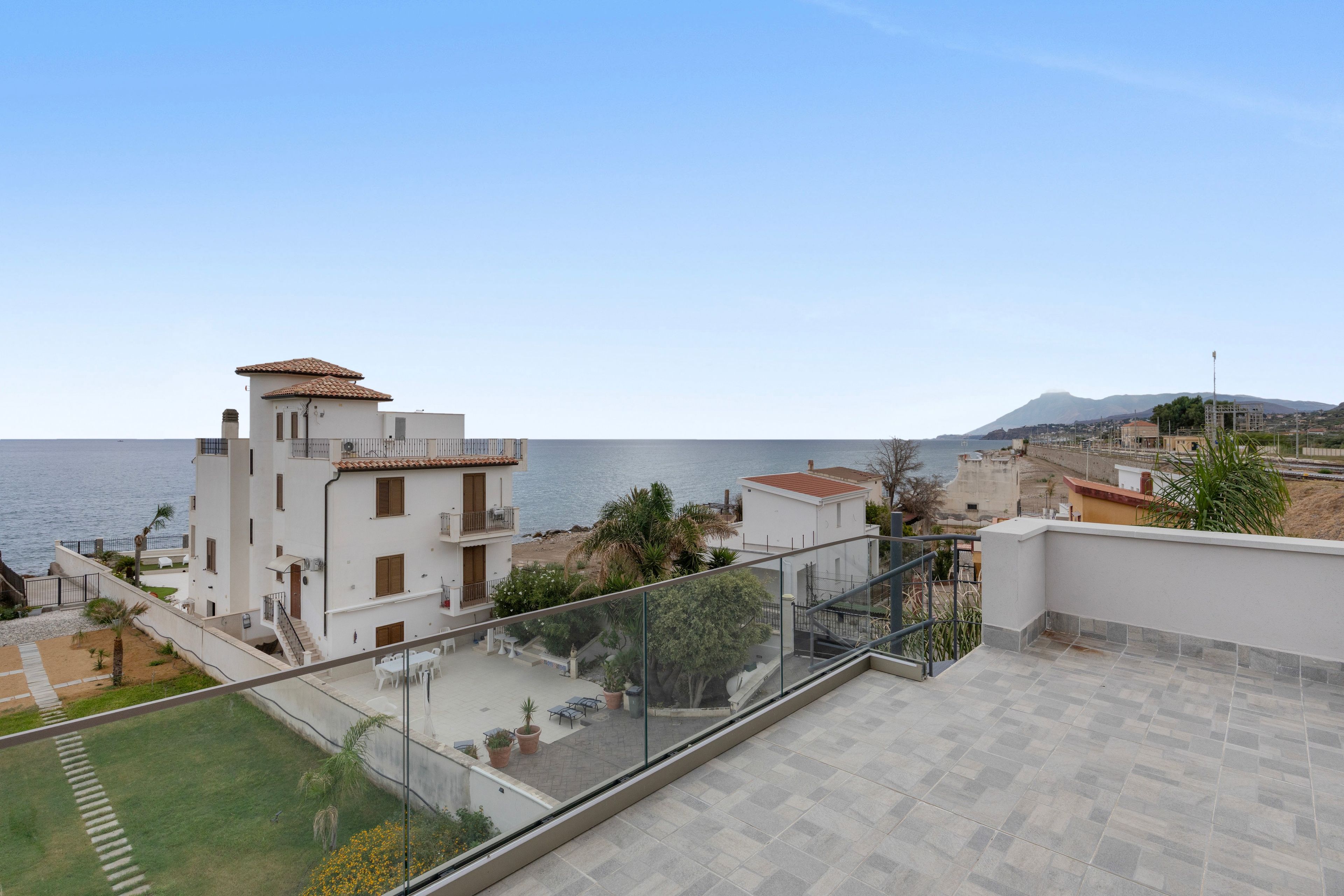 A residential area with a view of the sea, featuring a white building with a red-tiled roof and a balcony overlooking the ocean.