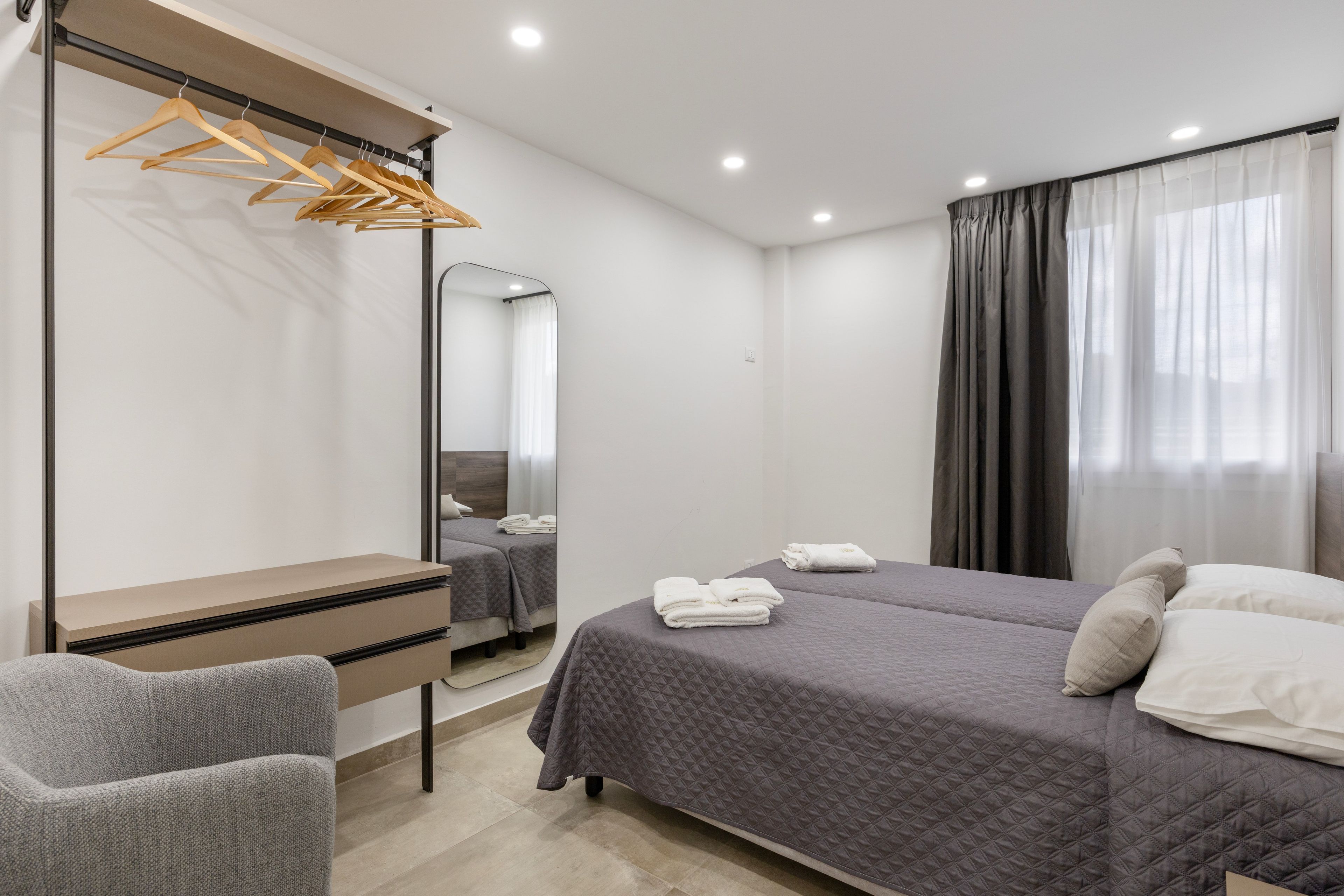 Una camera d'albergo con un letto, una scrivania, una sedia, uno specchio e un armadio.