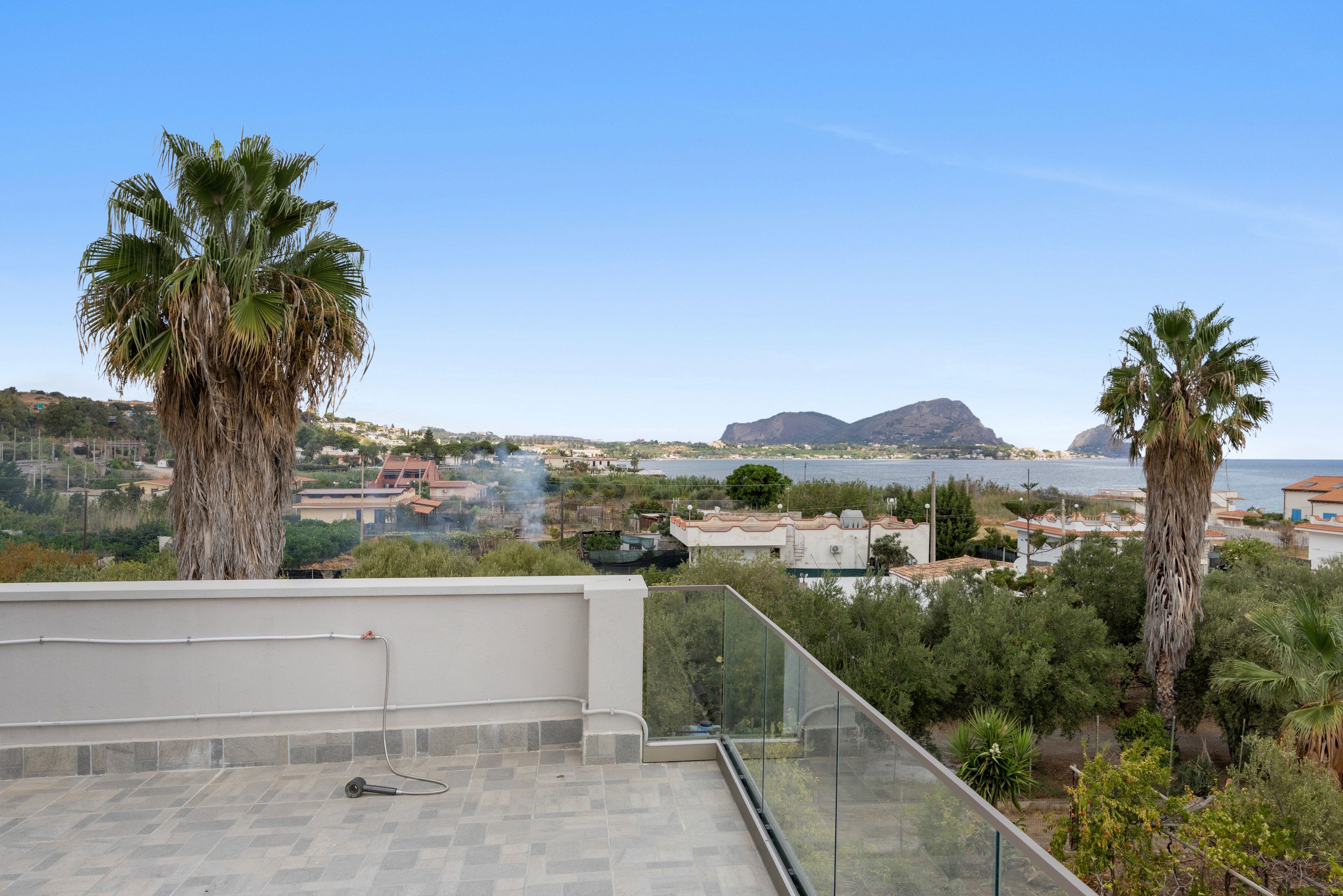A rooftop terrace with a clear view of a coastal town, palm trees, and a distant mountain.