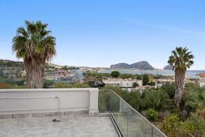 A rooftop terrace with a clear view of a coastal town, palm trees, and a distant mountain.