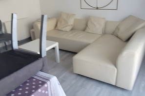 Una sala moderna con un sofá seccional color beige, una mesa de centro blanca y un mueble negro.