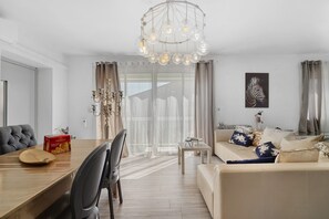 A modern living room with a dining area, a chandelier, and a sofa with decorative pillows.