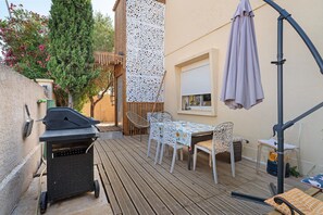 An outdoor patio with a grill, a table with chairs, and a pergola with a canopy.