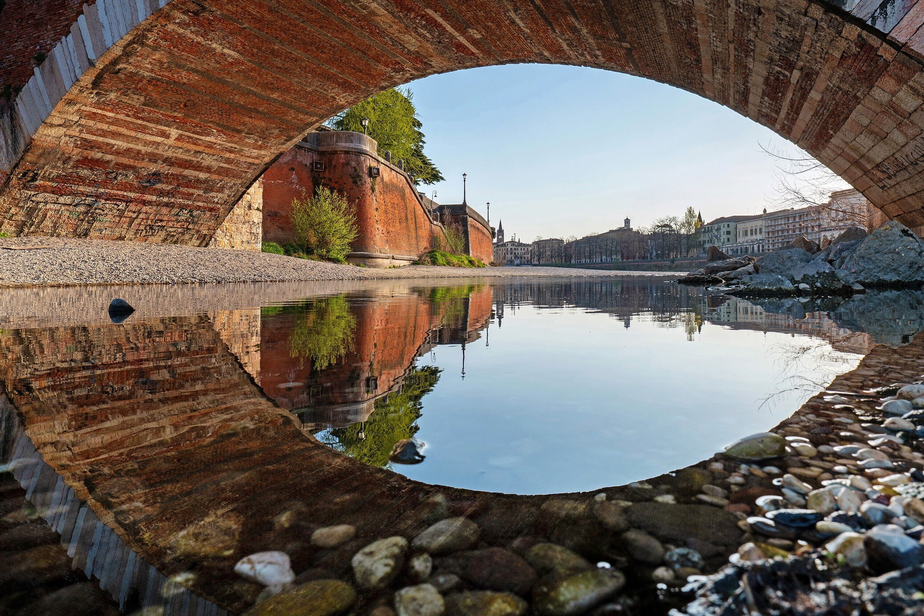 Eine Brücke mit deutlicher Spiegelung im Wasser, ein Steinweg und ein ruhiger Fluss.