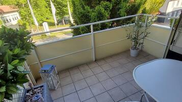 A balcony with a table and chairs, potted plants, and a view of trees and buildings.