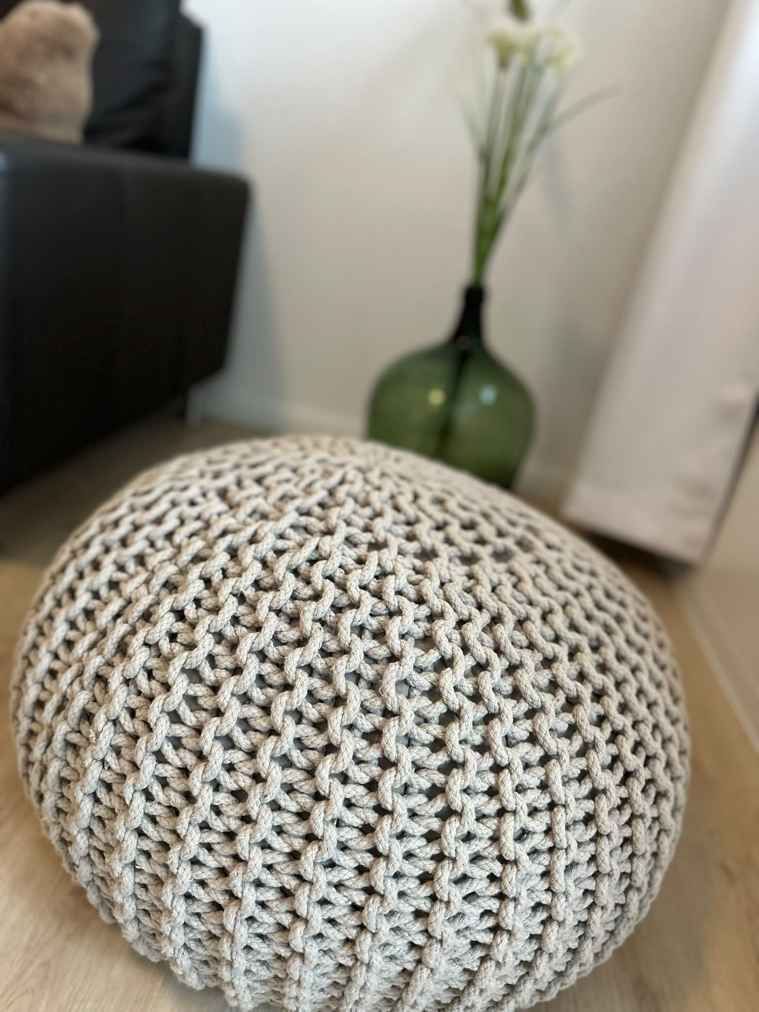 Een ronde, gebreide poef met een reliëfpatroon, op een houten vloer.