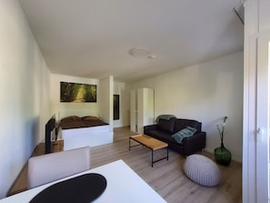 Ein modernes Wohnzimmer mit einer Couch, einem Couchtisch, einem Bett und einem Bild an der Wand.