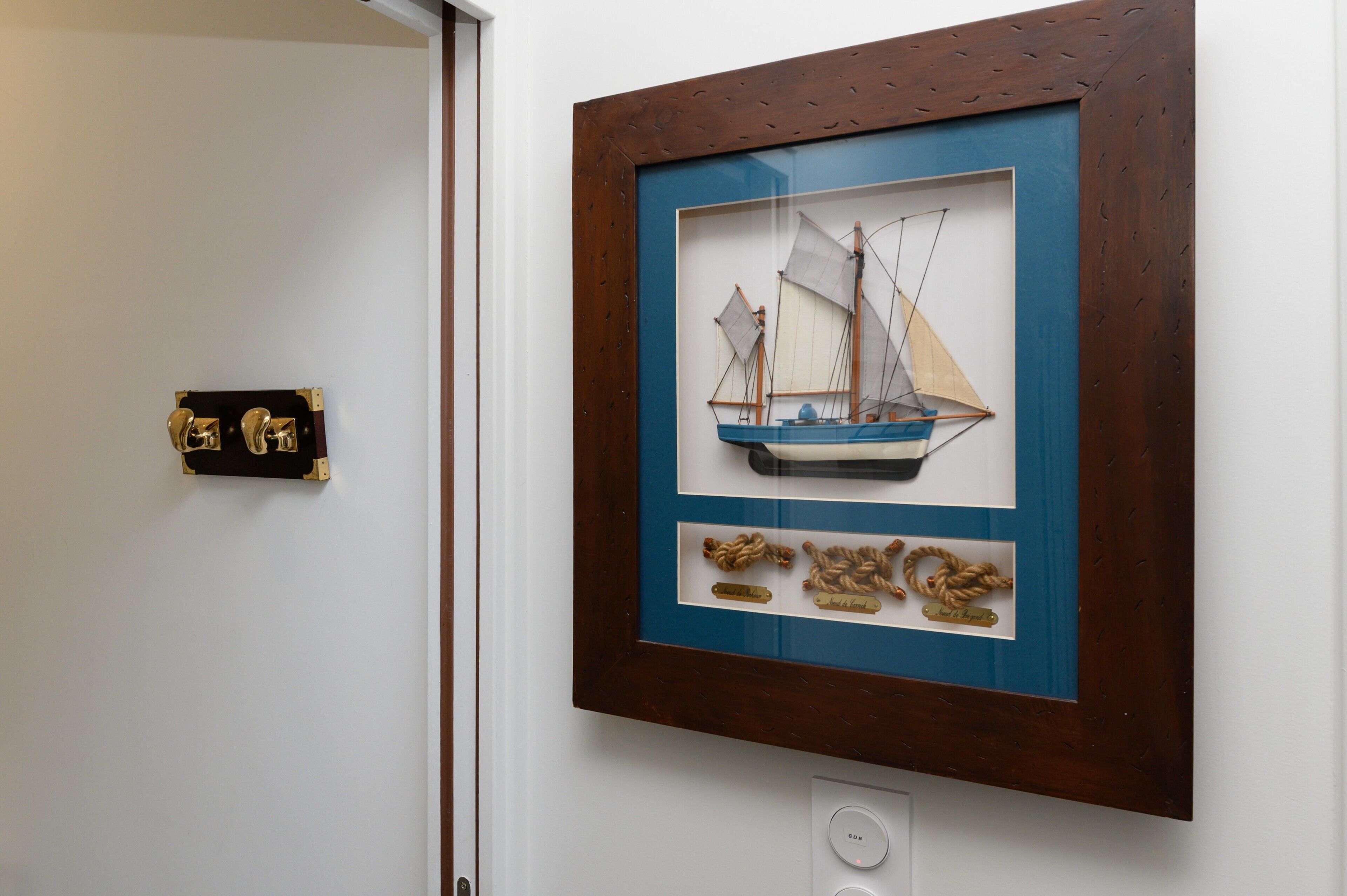 Modelo náutico enmarcado con un barco y cuerdas, colgado en una pared.