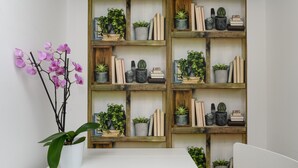 Una mesa blanca con una planta en maceta y una estantería de madera con plantas y libros.