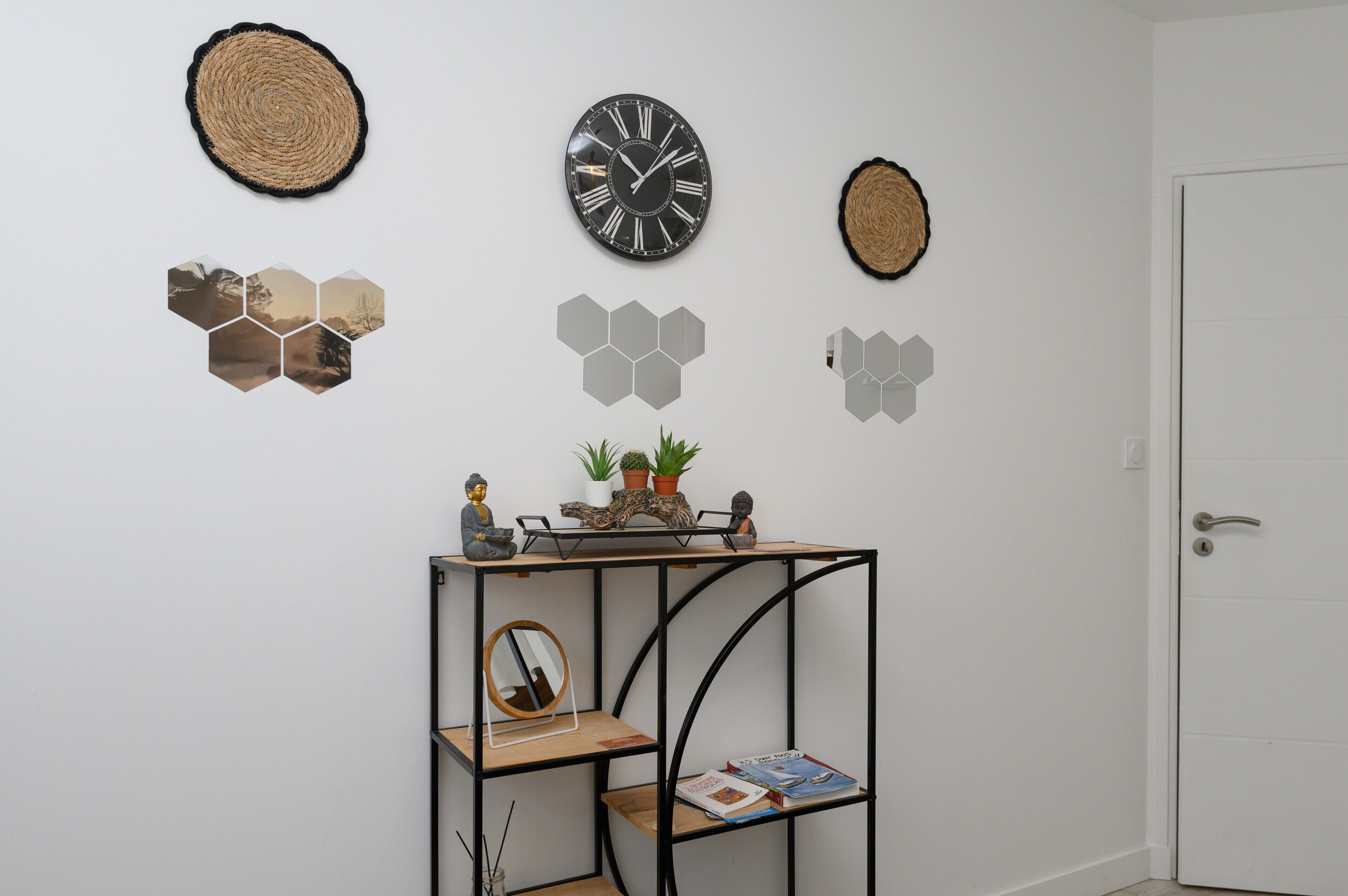 A wall with a clock, hexagonal mirrors, a small shelf with plants, and a door.