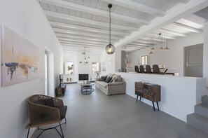 Een ruime woonkamer met een hoge plafond, een bank, een salontafel en een eethoek met stoelen.