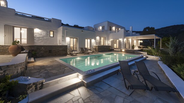 Ein modernes Haus mit Swimmingpool, Steinböden und Sitzgelegenheiten im Freien.