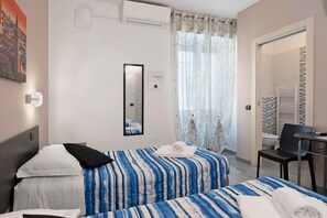 A hotel room with two beds, a desk, a chair, a mirror, and a bathroom visible through an open door.