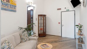 A living room with a sofa, a coffee table, a wooden cabinet, a TV mounted on the wall, and a door with an exit sign. - Room 'Farfalle' with Mountain View, Wi-Fi and Air Conditioning (Bastia)