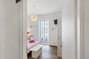 Quarto com cama, um banco, luminária pendente, porta e janela.