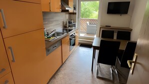 A modern kitchen with orange cabinets, a dining area with black chairs, and a TV mounted on the wall. - Apartment "New Holiday Home for 2 Guests" with Shared Garden, Balcony & Wi-Fi (Oelsnitz/Erzgebirge)