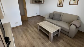 A modern living room with a wooden floor, a sofa, a coffee table, and a ceiling light fixture. - Apartment "New Holiday Home for 2 Guests" with Shared Garden, Balcony & Wi-Fi (Oelsnitz/Erzgebirge)