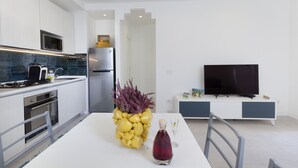 A modern kitchen with white cabinets, a stainless steel refrigerator, a microwave, and a dining area with a white table and chairs. - Casa Apreda in the Heart of Sorrento, Steps from the Sea (Sorrento)