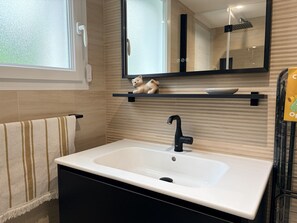 A bathroom with a white sink, black faucet, and a mirror above. - Appartement des Camélias – 100m from the Beach (La Tranche-sur-Mer)