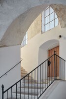 Una escalera con una puerta de madera al final, una pared blanca y una ventana con diseño de cuadrícula.