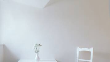 A white table with a vase and a chair in a room with white walls and wooden flooring.