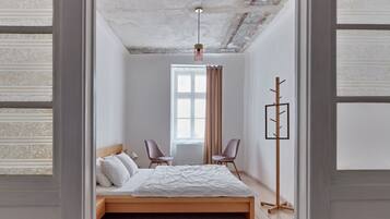 Un dormitorio con una cama de madera, dos sillas, una lámpara de pie y un ventanal con cortinas.